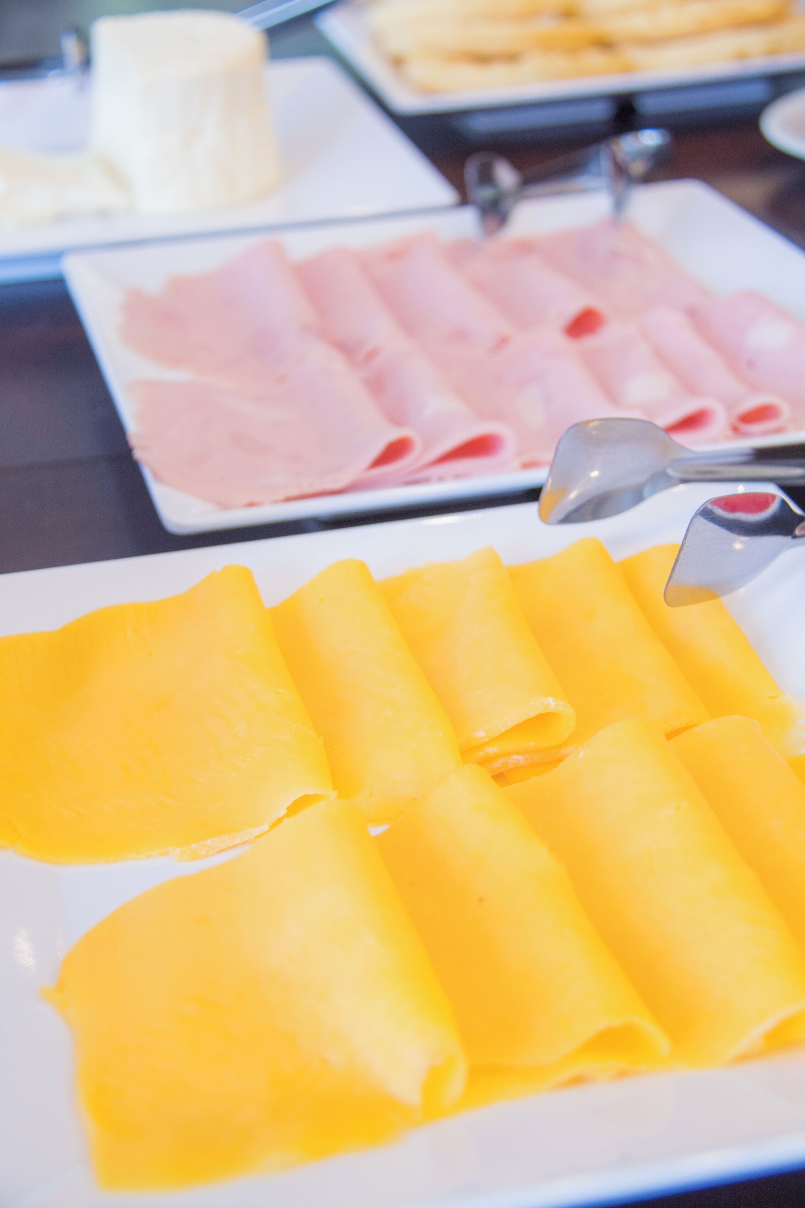 A buffet with various food items including cheese, ham, and a plate of yellow crepes.