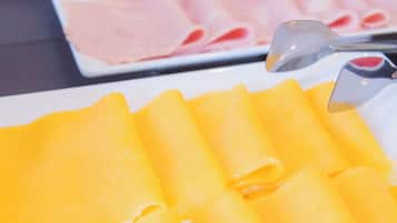 A buffet with various food items including cheese, ham, and a plate of yellow crepes.