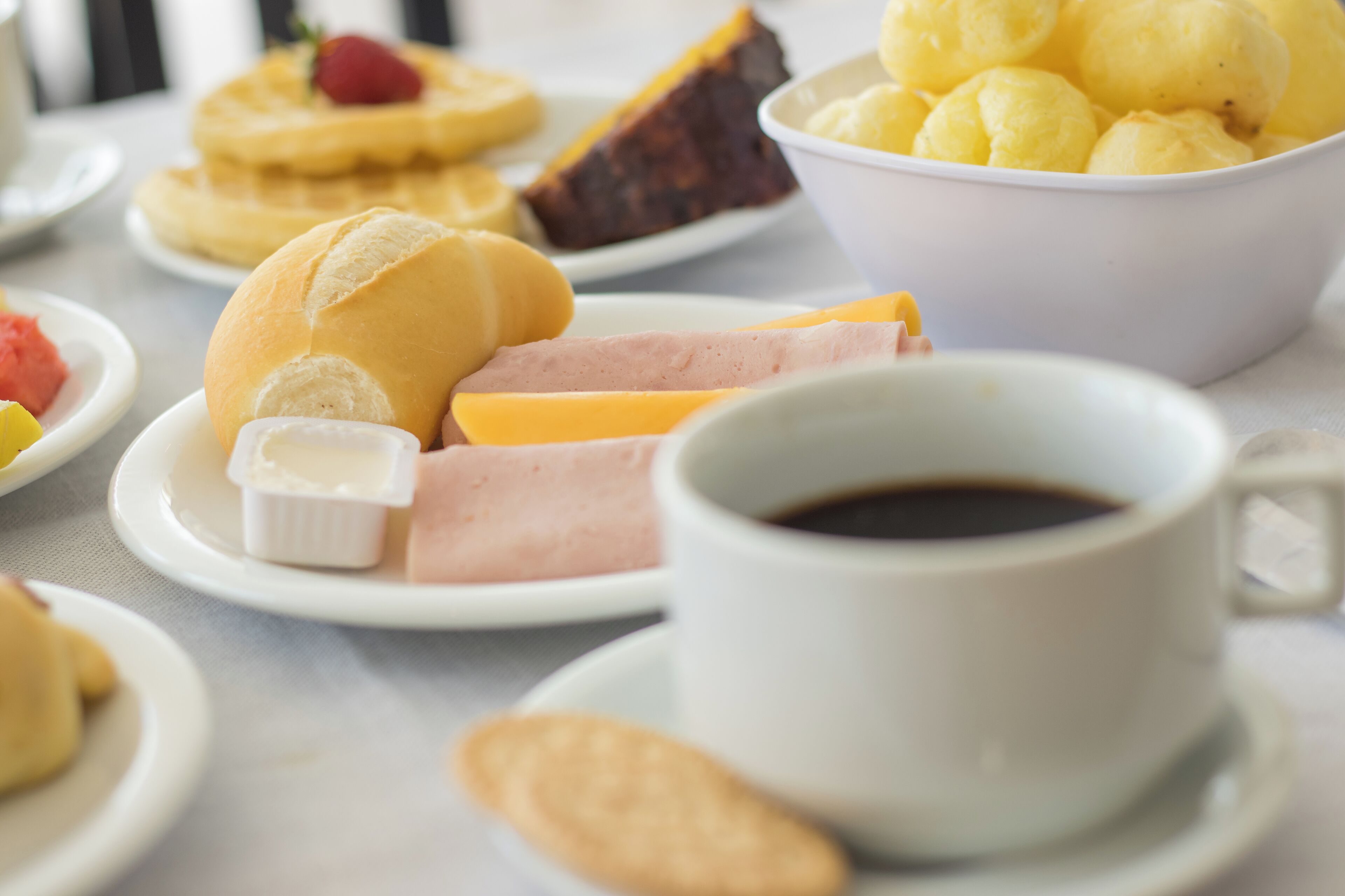 Een tafel met diverse ontbijtartikelen, zoals pannenkoeken, wafels, een fruitschaal en een kop koffie.