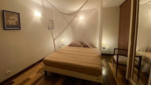 Een slaapkamer met een bed, bedlampen, een nachtkastje, een stoel en een raam met jaloezieën.