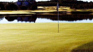 A golf course with a flagstick in the foreground, a pond in the middle, and a building in the background. - 2 Person Holiday Park Home in Testby (Malmö)