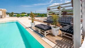 A poolside area with wooden loungers and planters. - Villa Frarogi by Rentbeat (Ostuni)