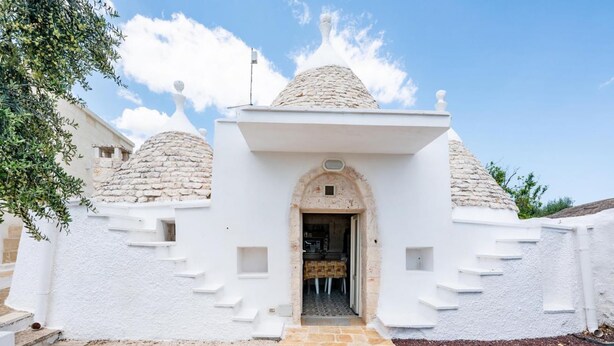 A building with a stone dome roof, a central entrance, and a stone staircase leading to the entrance. - Villa Frarogi by Rentbeat (Ostuni)