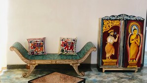 A green sofa with two decorative pillows, a small square table, and a cabinet with religious paintings. - 3-bedroom house in Kandy City with WiFi, AC (kandy)