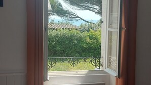 A bedroom with a large bed, a window with curtains, and a view of greenery and a building outside.