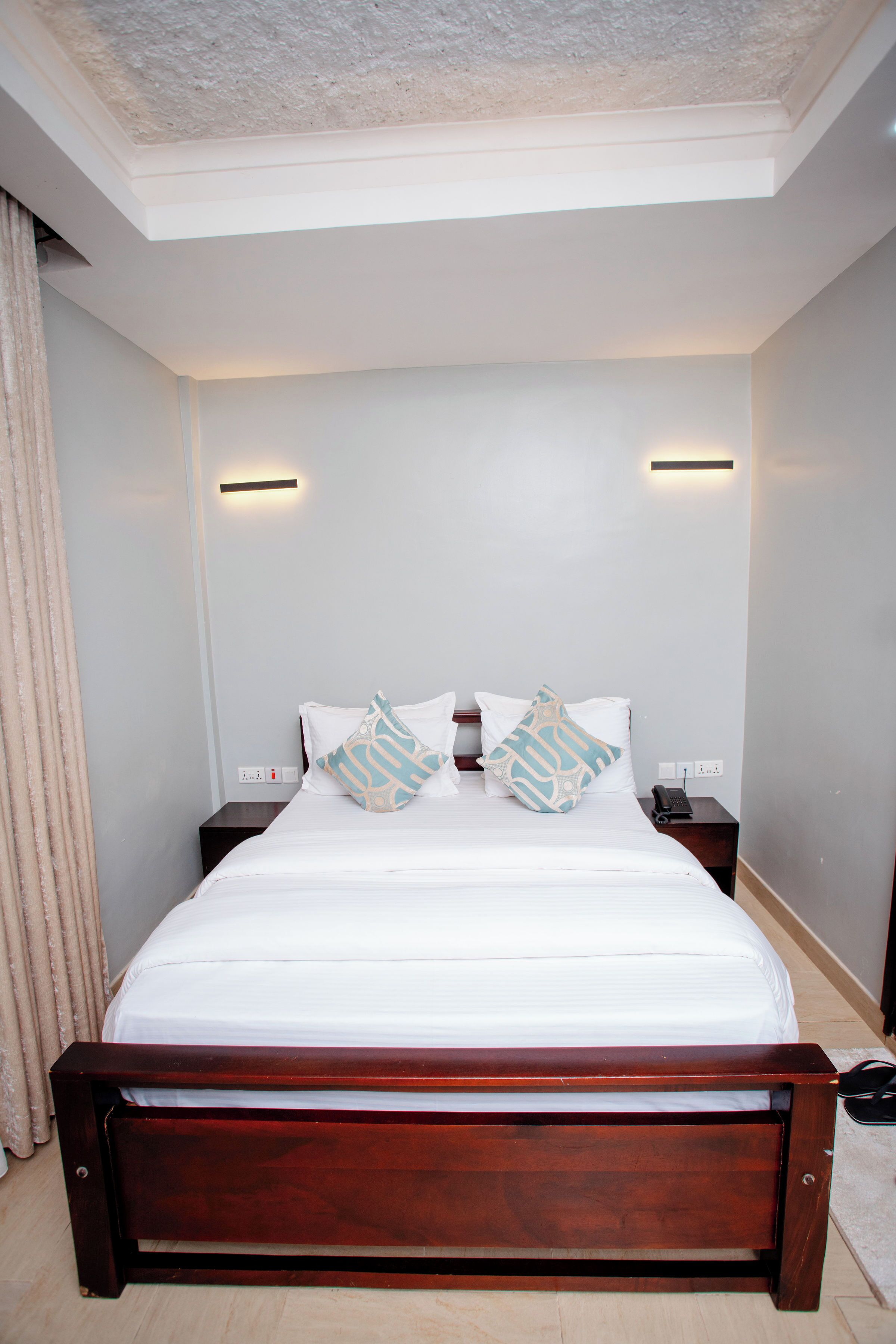 A neatly made bed with white linens and patterned pillows, a wooden headboard, and bedside tables with lamps.