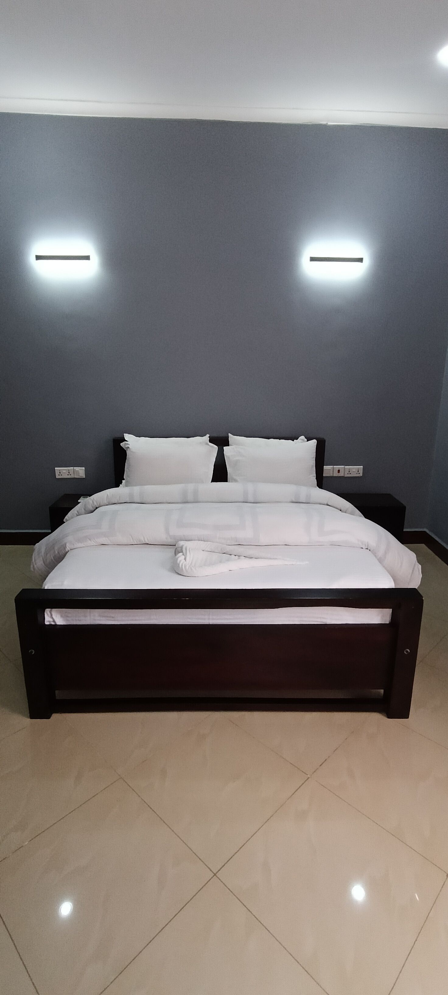 A large bed with a dark frame, white bedding, and two wall-mounted lights.
