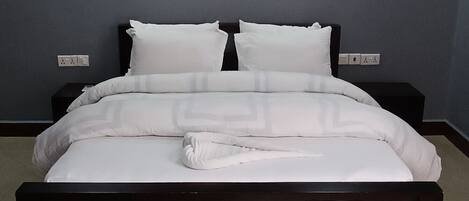 A large bed with a dark frame, white bedding, and two wall-mounted lights.