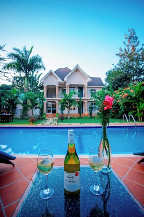 Une table au bord de la piscine avec une bouteille de vin et deux verres, une maison en arrière-plan et un ciel dégagé.