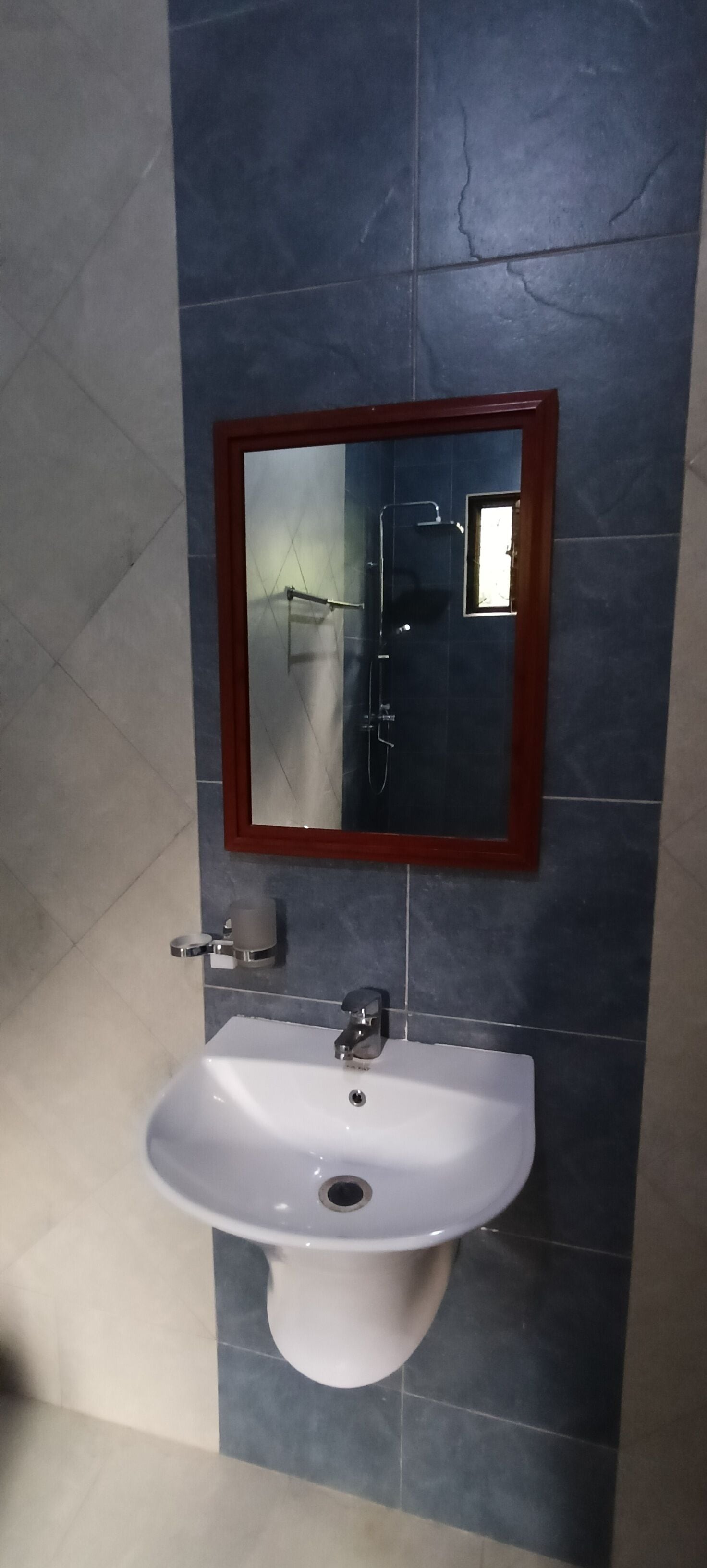 Un baño con lavamanos blanco, espejo con marco de madera y zona de ducha.