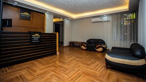 Uma área de recepção com piso de madeira em padrão herringbone, um balcão de recepção preto e um sofá preto.