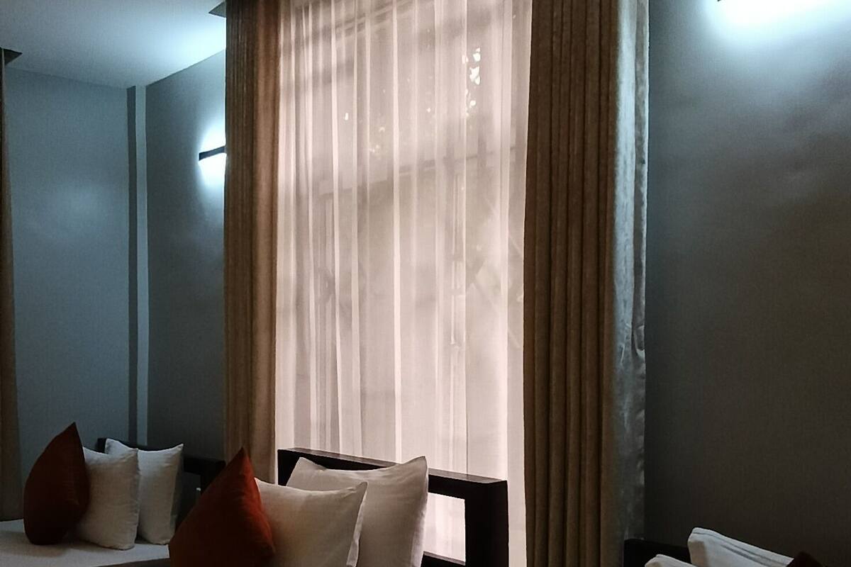 Ein Hotelzimmer mit zwei Betten, einem großen Fenster mit Vorhängen und einer Decke mit strukturierter Oberfläche.