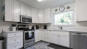 A modern kitchen with white cabinets, stainless steel appliances, and a large window providing natural light.