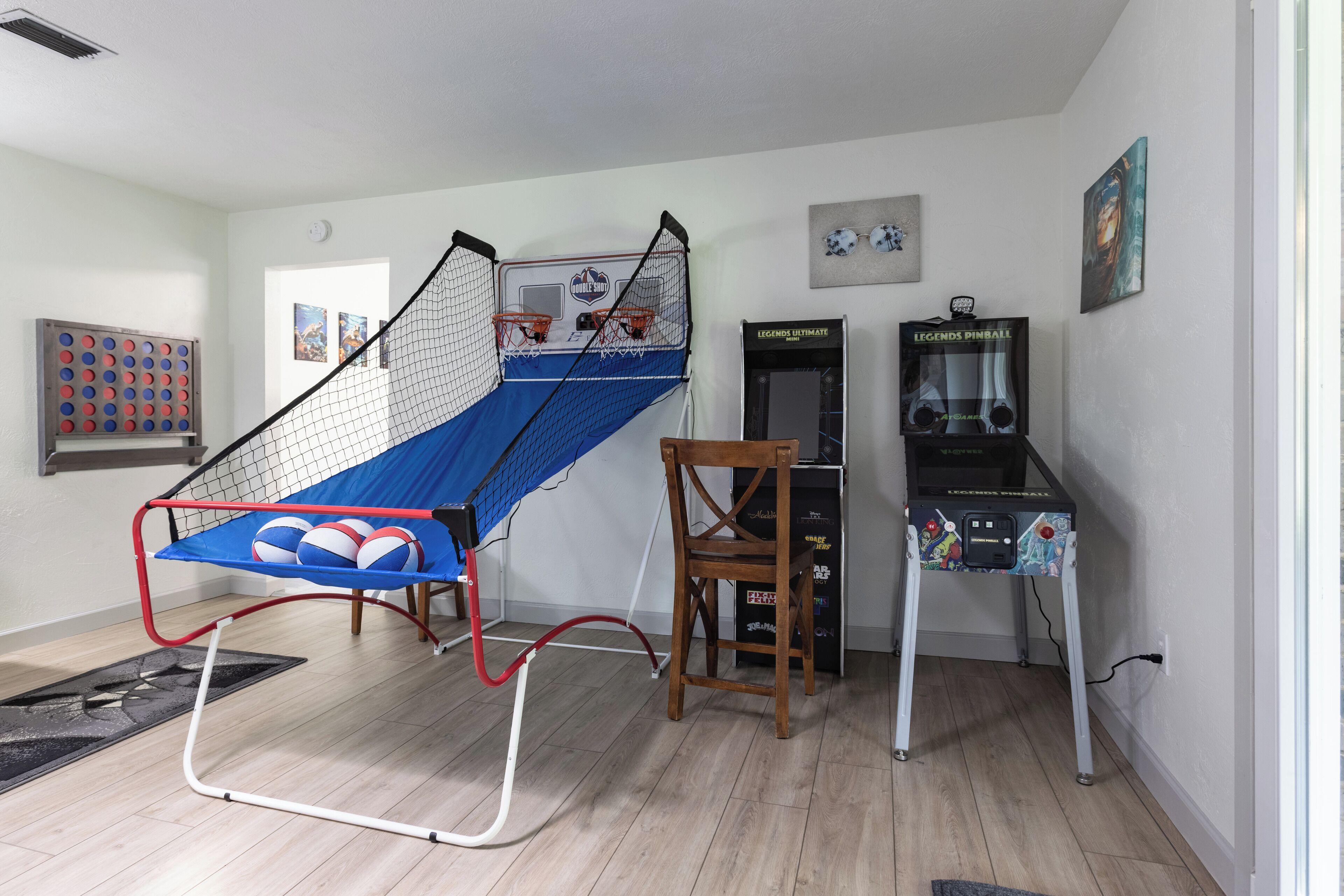 A room with a basketball hoop, a chair, and a pinball machine.