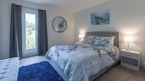 A bedroom with a bed, bedside tables, a window with curtains, a wall-mounted mirror, and a painting.