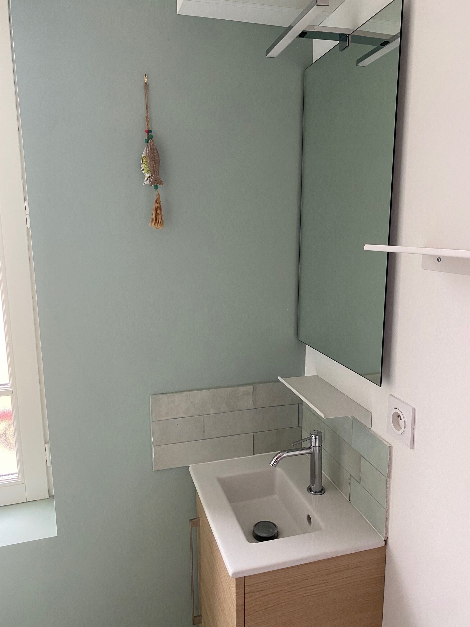 Een badkamer met een wit wastafel, een spiegel en een hangende decoratie.