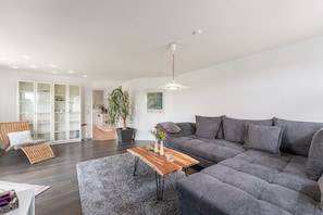 A modern living room with a grey sofa, a wooden coffee table, and a large window.