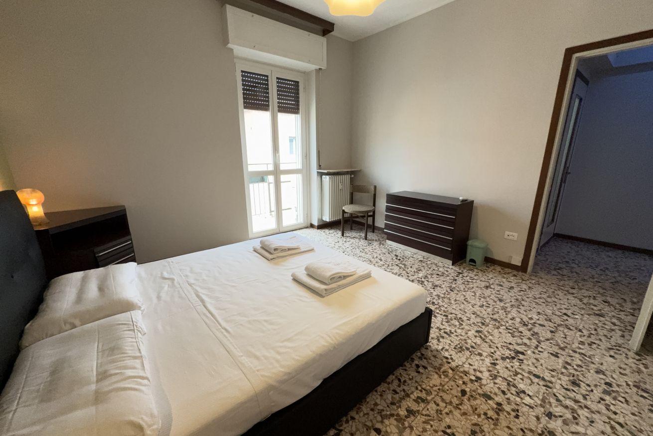 A bedroom with a bed, a radiator, a chair, and a window.