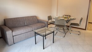 Un soggiorno moderno con un divano grigio, un tavolino da caffè con piano in vetro e un tavolo da pranzo con quattro sedie.