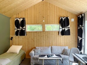 A room with wooden walls, a bed, a sofa, a table with a tray, and two windows. - 4 Person Holiday Home in Vaxholm (Vaxholm)