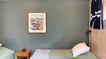 A room with two beds, a small table with a lamp, and a framed picture on the wall.