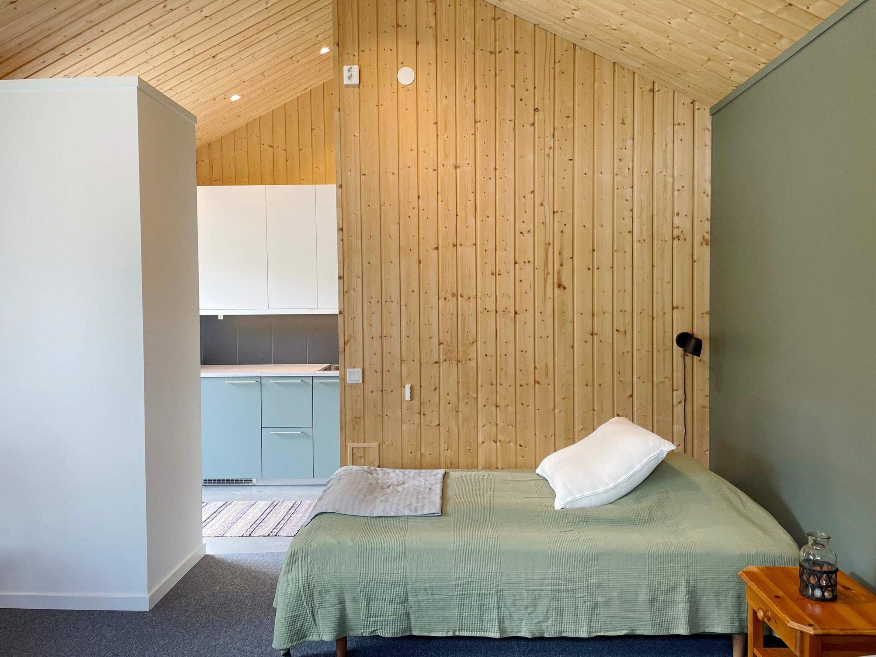 Quarto com cama, mesa de cabeceira e vista para uma cozinha.