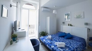A modern bedroom with a bed, a desk, and a chair. There is a window with a view of the outside. - At Giulia's Home Vomero Apt (NAPOLI)