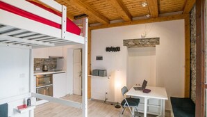 A compact room with a bunk bed, a kitchenette, a desk with a laptop, and a chair.