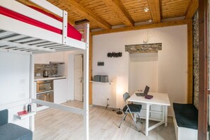Une petite pièce comprenant un lit superposé, un coin cuisine, un bureau avec un ordinateur portable et une chaise.