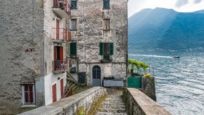A stone building with a staircase leading to a balcony overlooking a body of water and mountains.