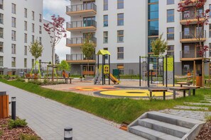 A playground with slides and climbing structures, surrounded by a landscaped area with benches and trees.
