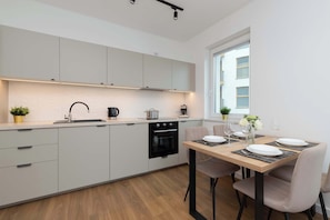 Une cuisine moderne avec des meubles blancs, un four noir et un coin repas comprenant une table et des chaises en bois.