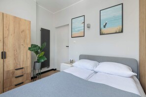 A bedroom with a bed, a wooden wardrobe, a potted plant, and two framed pictures on the wall.