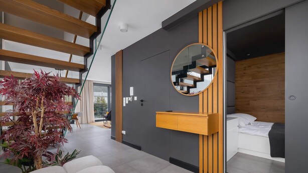 A modern bedroom with a bed, a bedside table, a mirror, and a staircase visible through an open door. - Spacious Apartment | Balcony | Parking | Mountain View (Szczyrk)
