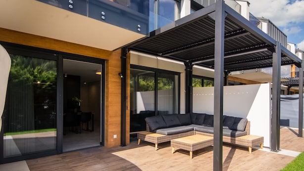 A modern outdoor living area with a sectional sofa, wicker furniture, and a pergola.
