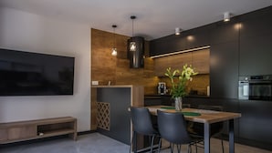 A modern kitchen with dark cabinetry, a wooden accent wall, and a dining area with a table and chairs.