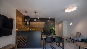 A modern kitchen with a central island, pendant lighting, and a flat-screen TV mounted on the wall.