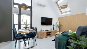 Ein modernes Wohnzimmer mit Essbereich, einem an der Wand befestigten Flachbildfernseher und einem großen Fenster mit Jalousien.