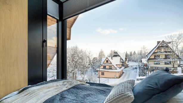 Ein Schlafzimmer mit einem großen Fenster mit Blick auf ein verschneites Dorf.