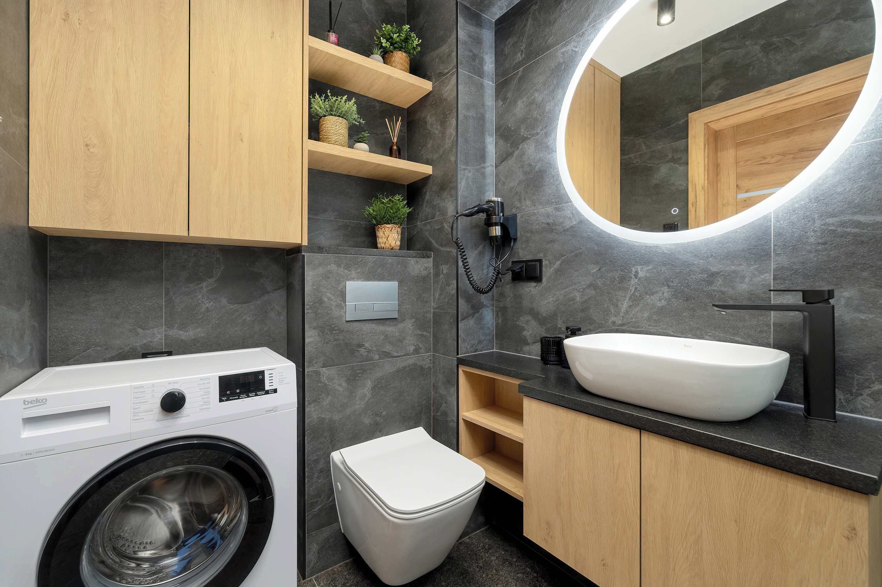 Ein modernes Badezimmer mit Waschmaschine, Toilette, Waschbecken und Spiegel.