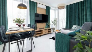 Un soggiorno moderno con zona pranzo, televisore a schermo piatto e divano con una coperta verde.