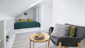 Un dormitorio acogedor en el ático con cama, un sillón gris y una mesita con un sándwich.