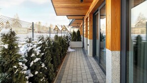 Un pasillo exterior cubierto con techo de madera, puertas de vidrio y un sendero cubierto de nieve.