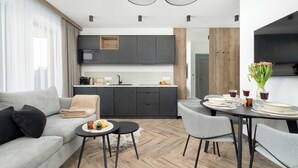 Una sala de estar moderna con un sofá gris, una mesa de comedor preparada para cuatro personas y una zona de cocina con armarios oscuros y un microondas.