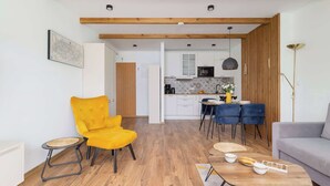 A modern kitchen with white cabinets, a wooden ceiling, and a dining area with a yellow chair and a grey sofa.