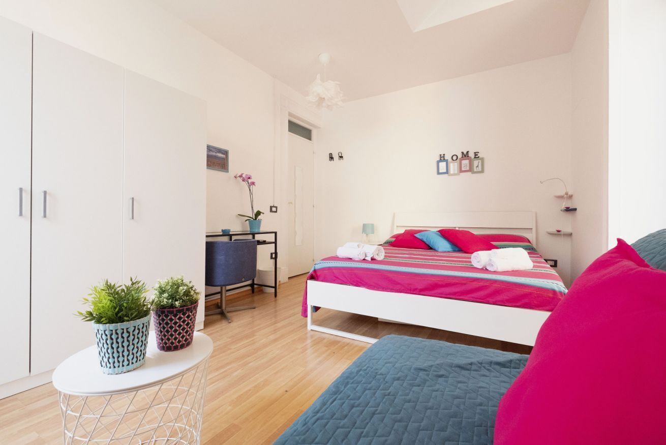 Une chambre à coucher comprenant un lit, un bureau, deux plantes en pot et une armoire.