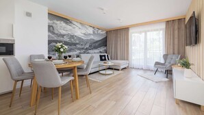 Een moderne woonkamer met een eethoek, een bank en een aan de muur bevestigde televisie.