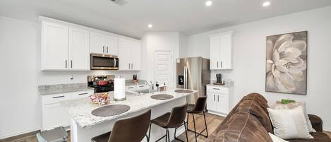 A modern kitchen with white cabinets, stainless steel appliances, and a central island with bar stools.