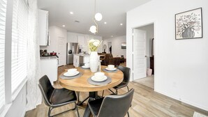 A modern kitchen with white cabinets, a dining table with chairs, and a vase with flowers. - Marice Serene Home at Katy Fulshear  (Fulshear)