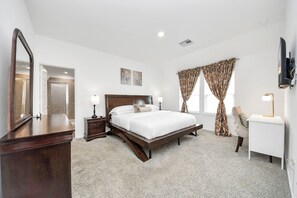 A bedroom with a bed, bedside tables, a desk, a chair, a large mirror, and a TV. - Marice Serene Home at Katy Fulshear  (Fulshear)
